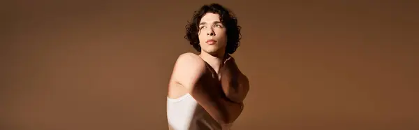A confident young man with curly hair showcases a stylish tank top in a studio environment, banner — Stock Photo