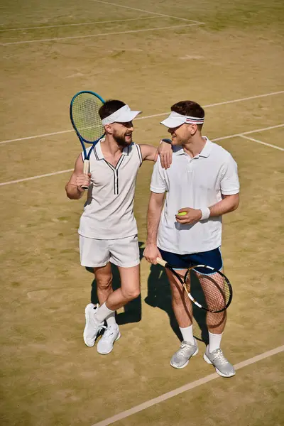 Pareja gay compartir un alegre momento en la pista de tenis después de un divertido partido bajo el sol. - foto de stock