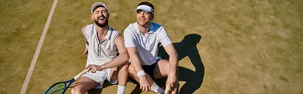 Two young men laugh after tennis game on a sunny summer day, sharing joy and sport, banner — Stock Photo