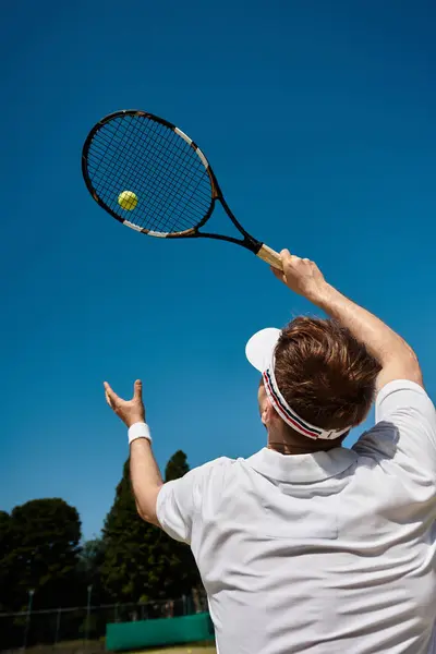A skilled player in white serves under a clear blue sky, embodying summer tennis. — Stock Photo