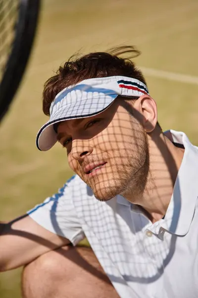 Un hombre en ropa deportiva blanca muestra sus habilidades mientras juega al tenis en un día soleado de verano. - foto de stock