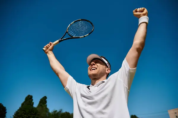 A joyful male tennis player raises his arms in triumph under a clear blue sky. — Stock Photo