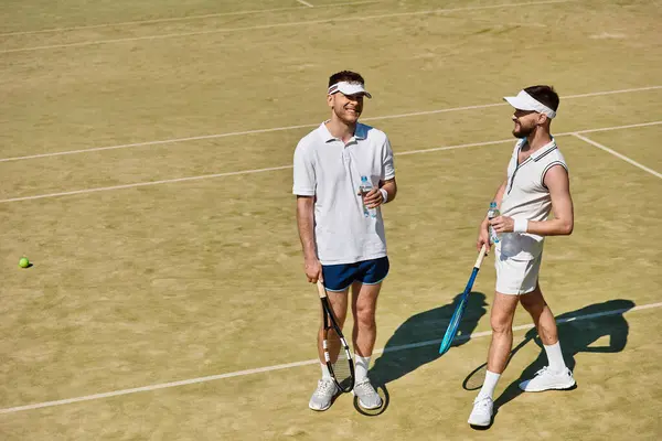 Two men enjoy a friendly match on a sunny tennis court, sharing laughter and sportsmanship. — Stock Photo