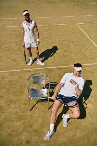 Dos hombres guapos participan en un intenso partido de tenis en una cancha soleada, llena de emoción. - foto de stock