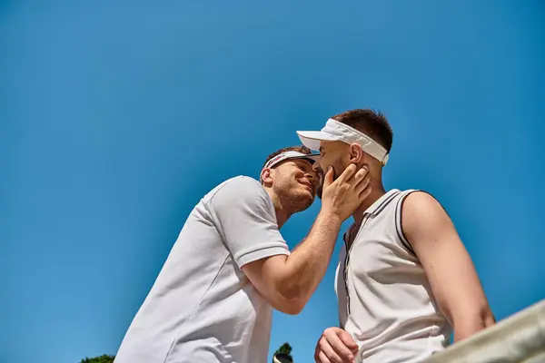 Two men share an affectionate kiss while playing tennis on a sunny summer day. — Stock Photo