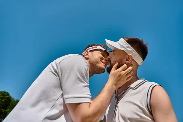 Two young men share a sweet moment on the tennis court during a sunny summer day. — Stock Photo