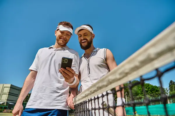 Two men share a light moment on a sunny tennis court during their summer game. — Stock Photo