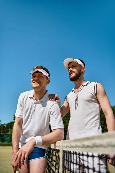 Two men on a tennis court share smiles and laughter while enjoying their game in the summer sun. — Stock Photo
