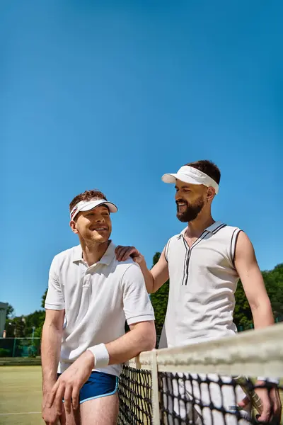 Two men play tennis on a sunny summer day, sharing smiles and laughter on the court. — Stock Photo