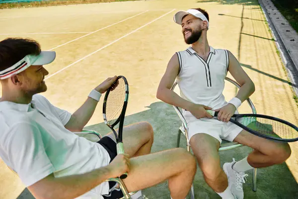 Two men share laughter and excitement during a fun tennis break on a warm day. — Stock Photo