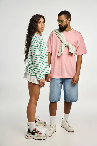 Couple holding hands in trendy outfits, exuding love and confidence against a plain background — Stock Photo
