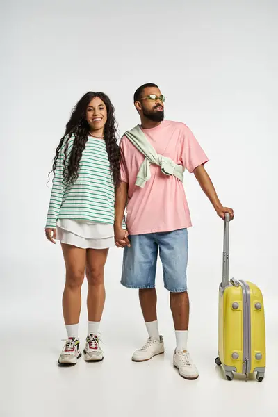 Couple stands together with a suitcase, radiating love and style against a soft background. — Stock Photo