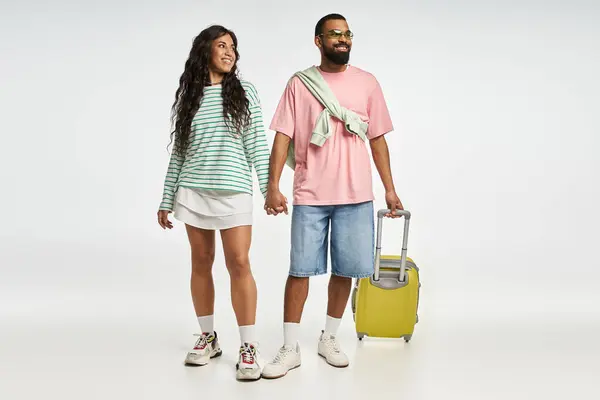 A fashionable couple stands together, smiling and holding hands, ready to explore new destinations. — Stock Photo