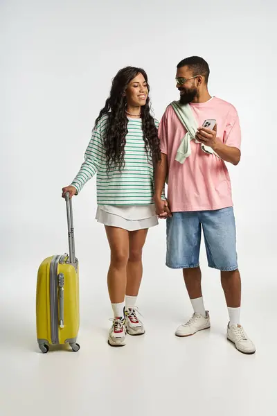A fashionable couple holds hands and smiles, preparing for a fun trip in a bright studio. — Stock Photo