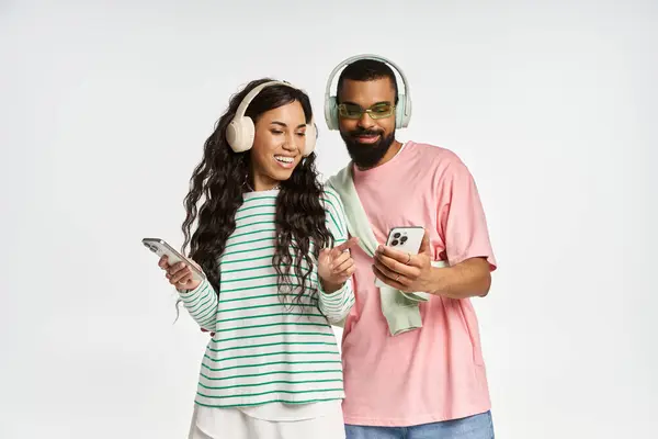 Casal compartilha um momento alegre como eles ouvem música em seus dispositivos, irradiando amor e estilo. — Fotografia de Stock
