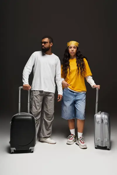 Trendy couple stands confidently with luggage, ready for adventure in a modern studio. — Stock Photo