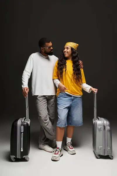 A fashionable man and woman smile at each other while holding their luggage, ready to travel. — Stock Photo