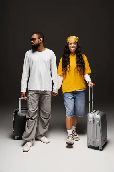 A fashionable couple holds hands while standing with their suitcases, ready for travel. — Stock Photo