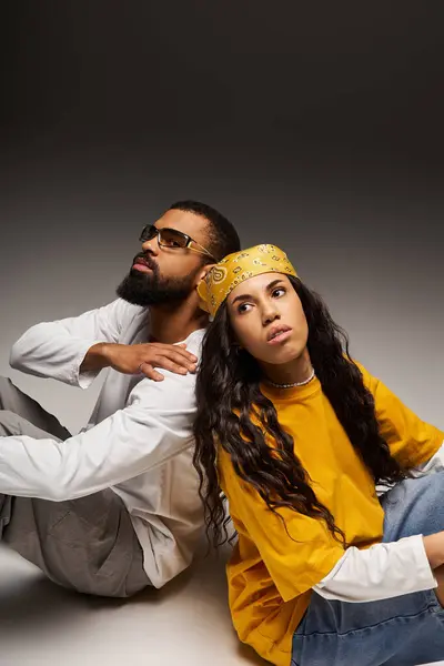 A trendy couple sits back to back, showcasing their unique style and connection. — Stock Photo