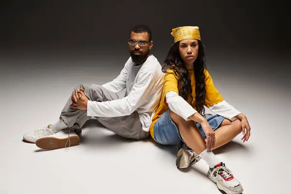 A stylish couple sits back to back, highlighting their fashion sense and connection. — Stock Photo