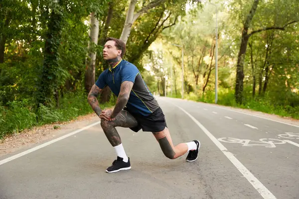 A handsome young man stretches on a peaceful pathway lined with trees, enjoying nature and fitness. — Stock Photo