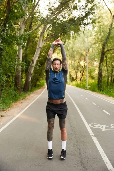 A handsome young man takes a peaceful walk, stretching his arms under the green canopy of trees. — Stock Photo