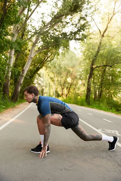 Un beau jeune homme s'étire et se prépare à courir dans une rue paisible entourée d'arbres. — Photo de stock