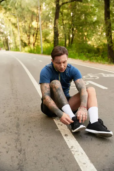 Un hombre joven y en forma disfruta de un tranquilo paseo a lo largo de un sendero arbolado, atándose los zapatos. - foto de stock