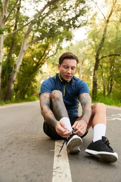 A handsome young man takes a moment to tighten his shoelaces while enjoying a serene walk in nature. — Stock Photo