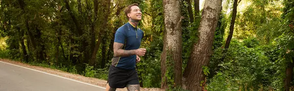 A fit young man walks along a serene path, surrounded by lush greenery and tall trees. — Stock Photo