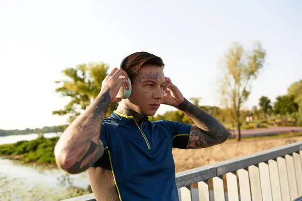 A young man with tattoos walks along a riverside path, listening to music and soaking in the sun. — Stock Photo