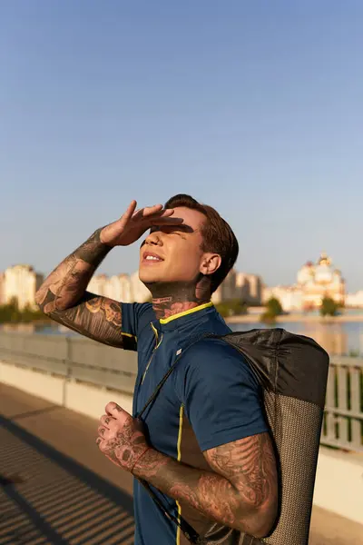 A young man wearing a blue shirt strolls alongside a serene waterfront under a bright sky. — Stock Photo