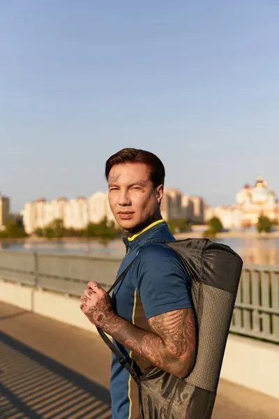 Молодой человек с татуировками прогуливается в солнечный день, демонстрируя свой стиль у воды. — стоковое фото