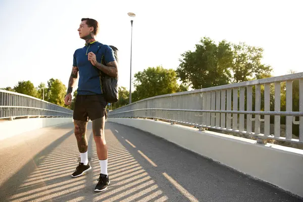 A young, stylish man strolls across a bridge, embracing the warm sunlight on a peaceful day. — Stock Photo