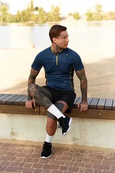 A handsome young man sits on a bench during a leisurely stroll by the water with bright sunshine. — Stock Photo