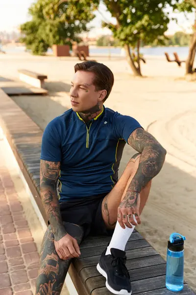 A young man with tattoos takes a moment to relax and enjoy the views by the water during his walk. — Stock Photo