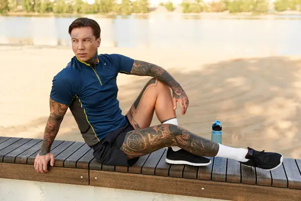 Young man with tattoos relaxes by the water, soaking in the tranquil evening atmosphere. — Stock Photo