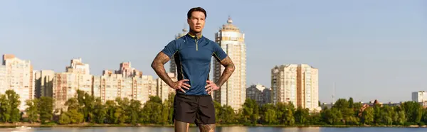 A young man stands confidently by the river, taking in the vibrant city views on a sunny day. — Stock Photo