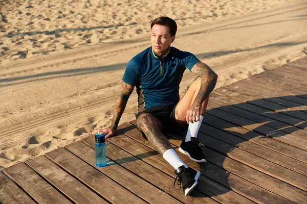 A young man relaxes in casual athletic wear, sitting on a wooden boardwalk by the beach. — Stock Photo