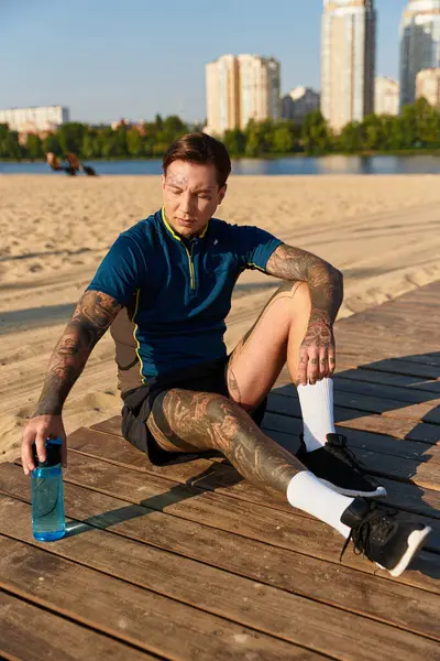 Handsome young man rests on wooden deck by the beach, enjoying a warm day and staying hydrated. — Stock Photo