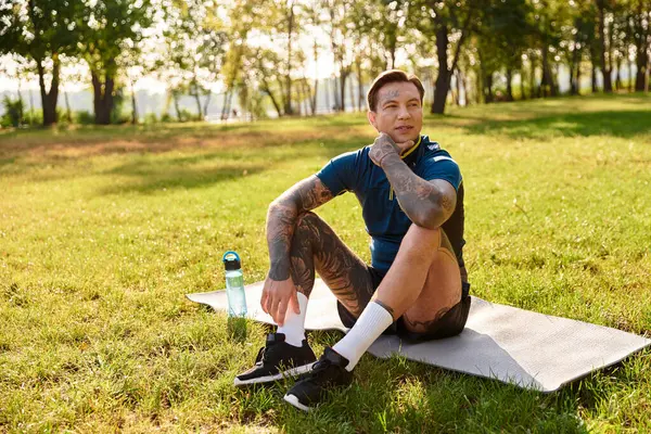 A charming young man sits on a mat, taking a breather during his leisurely walk in the park. — Stock Photo