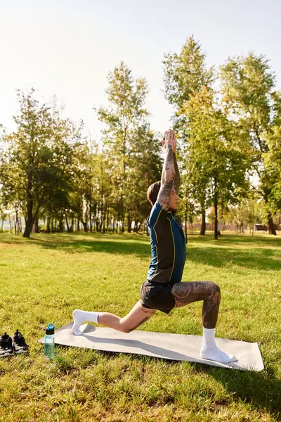 A handsome young man stretches in a yoga pose on a mat, enjoying the sunshine in a lush park. — Stock Photo