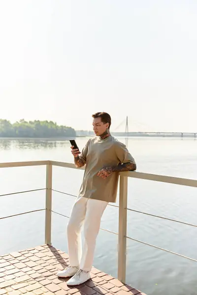 Handsome young man leans against a railing by the water, enjoying a sunny day on his stroll. — Stock Photo