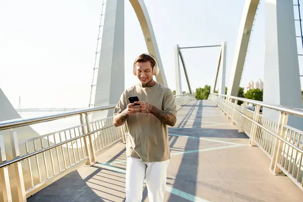 A young man with a cheerful smile walks casually on a modern bridge, immersed in his music. — Stock Photo