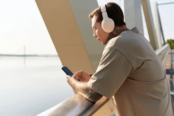 A young man strolls by the river, absorbed in music through his headphones while checking his phone. — Stock Photo