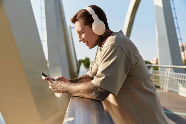 A handsome young man leans on the railing, smiling with headphones on. — Stock Photo