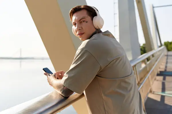 A young man strolls the riverfront in headphones, checking his phone on a sunny day. — Stock Photo