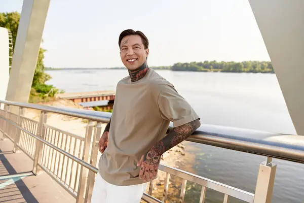 Handsome young man smiles while casually walking along the riverside path on a sunny day. — Stock Photo