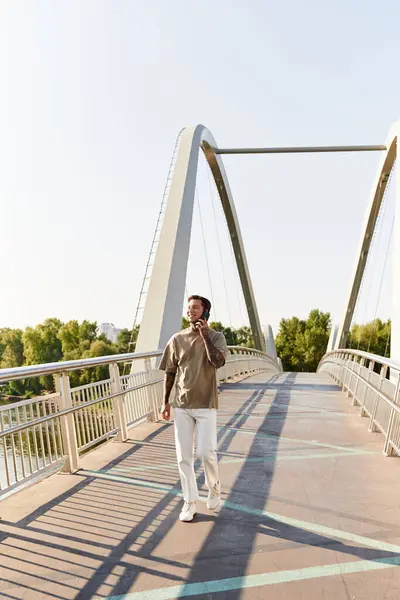 Красивий молодий чоловік неквапливо ходить через пішохідний міст в ясний день, розмовляючи по телефону. — Stock Photo