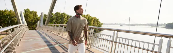 A charming young man walks leisurely across a bridge, basking in the warm sunlight by the river. — Stock Photo